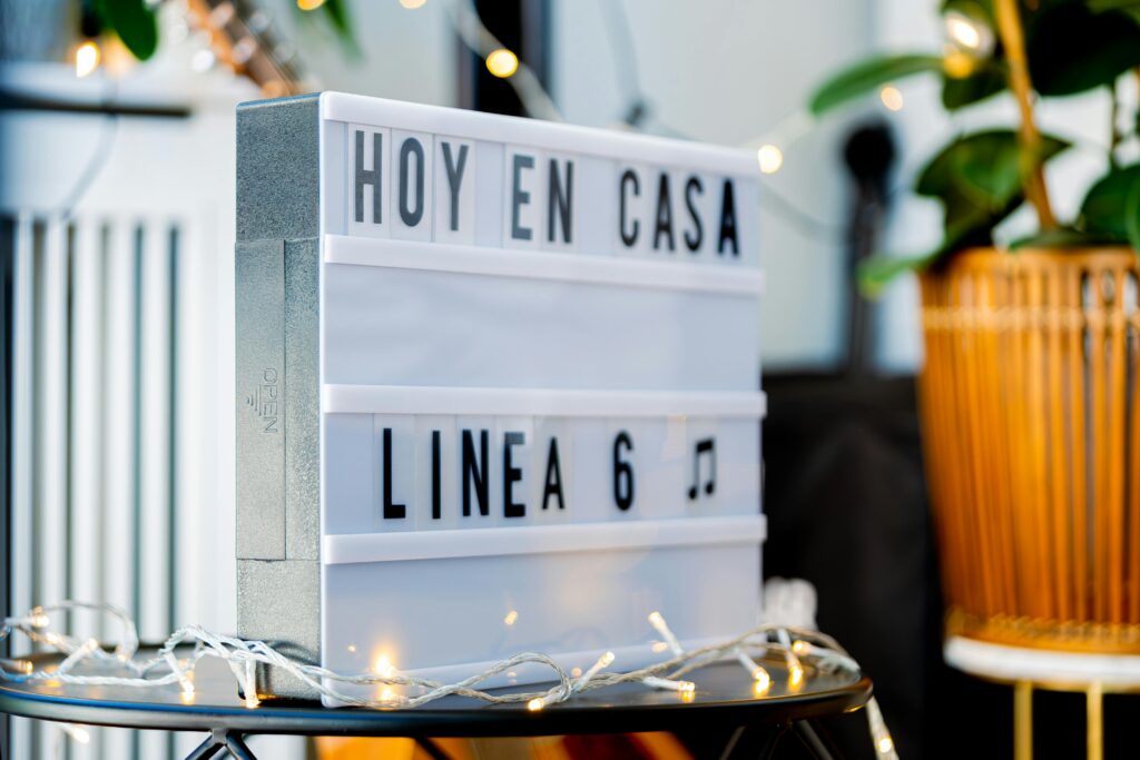 A cozy indoor setting featuring a lightbox sign with 'Hoy en Casa Linea 6' text, adorned with string lights.